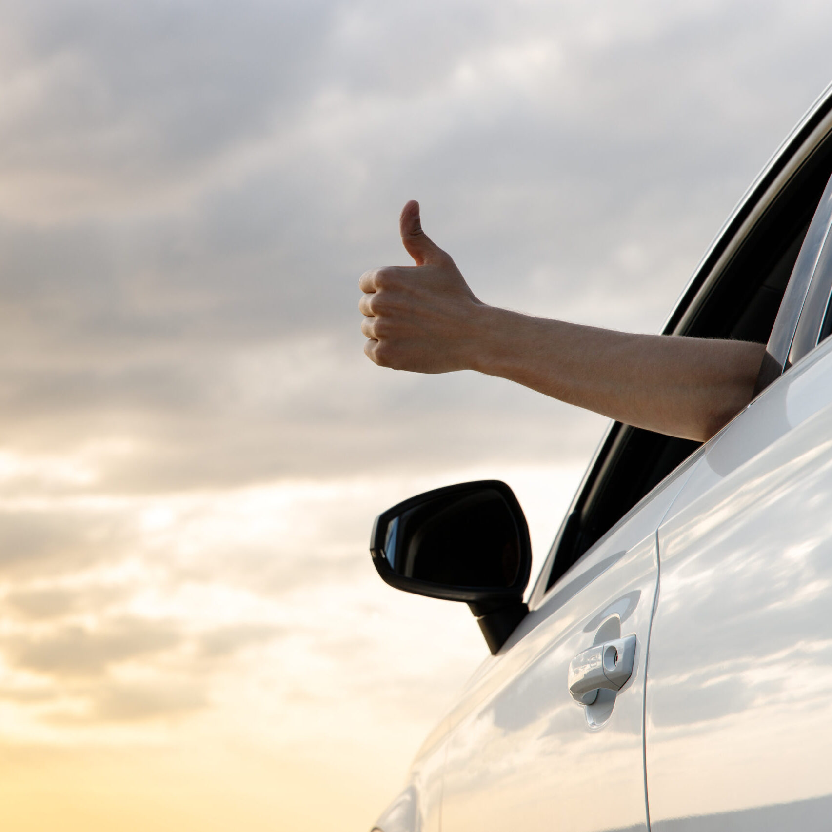 Man showing thumbs up sign out the window with a hand from inside the car. A sunset sky, relaxing, enjoying road trip and feeling the air and freedom. Toward adventure, vacation